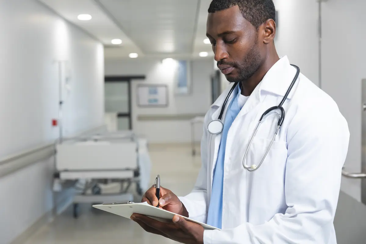 Doctor writing infection-control protocol notes on a clipboard in a hospital corridor